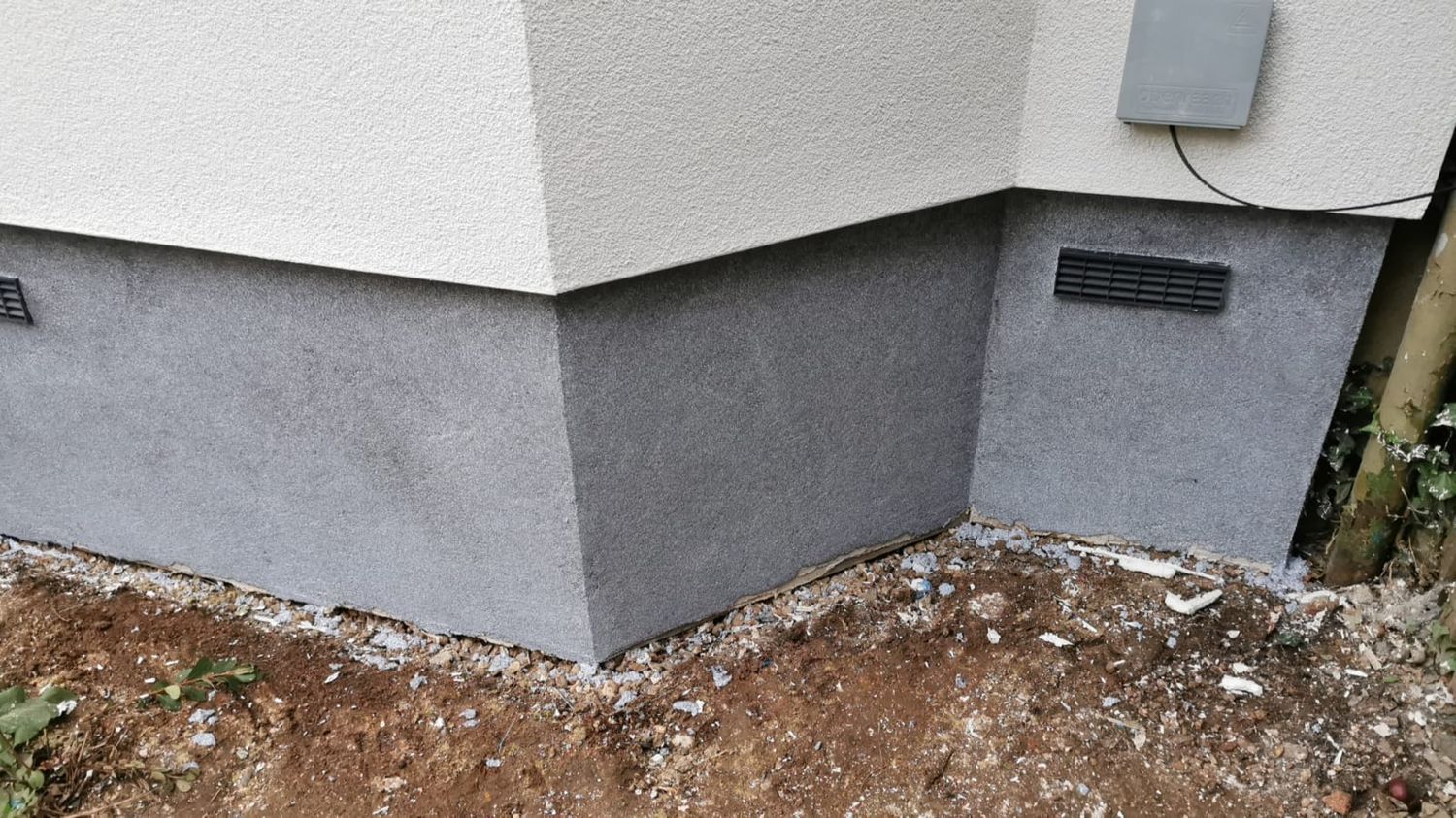 Grey mosaic render over plinth insulation with ventilation grilles